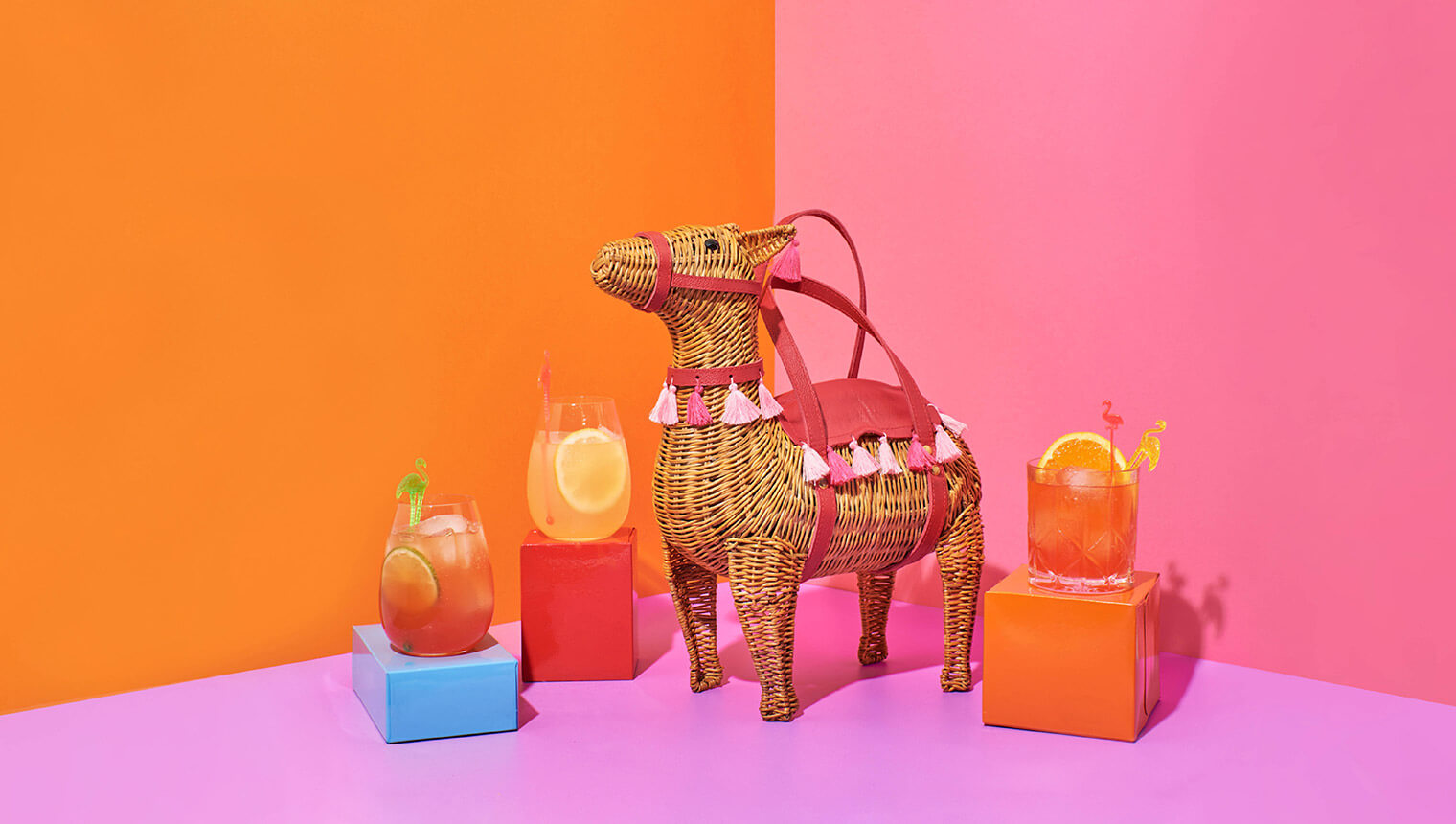 Bright orange and pink scene with llama shaped wicker handbag surrounded by cocktails