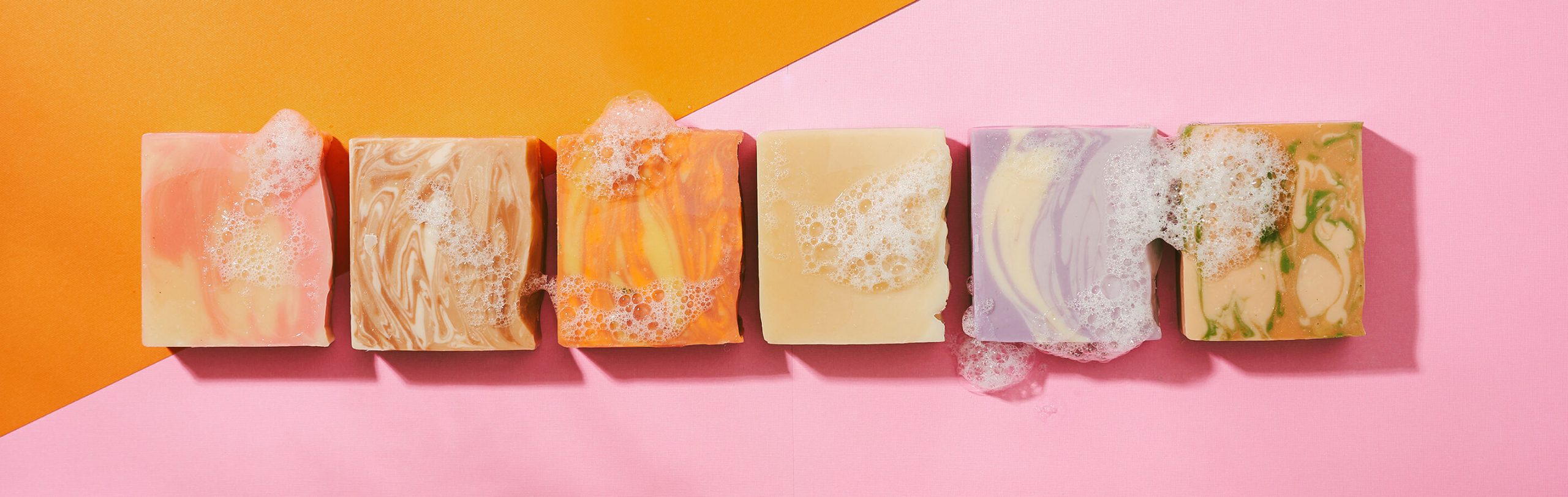 A line up of Brand The Boldest Co’s soap bars on a pink/orange paper background