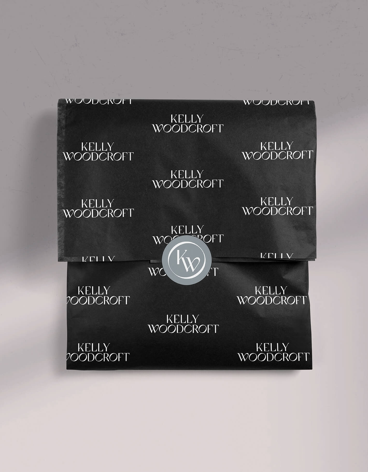 Custom tissue paper design with the kelly woodcroft logo and a custom sticker seal sits in a grey background