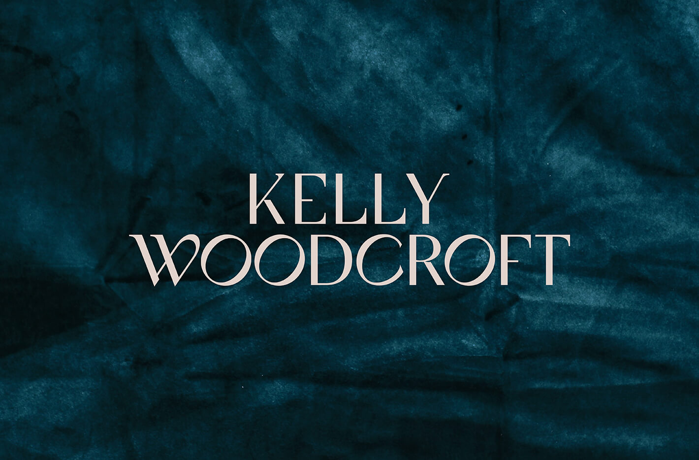 The custom jewellery designer logo for Kelly Woodcroft is in white on a shadowy teal velvet background