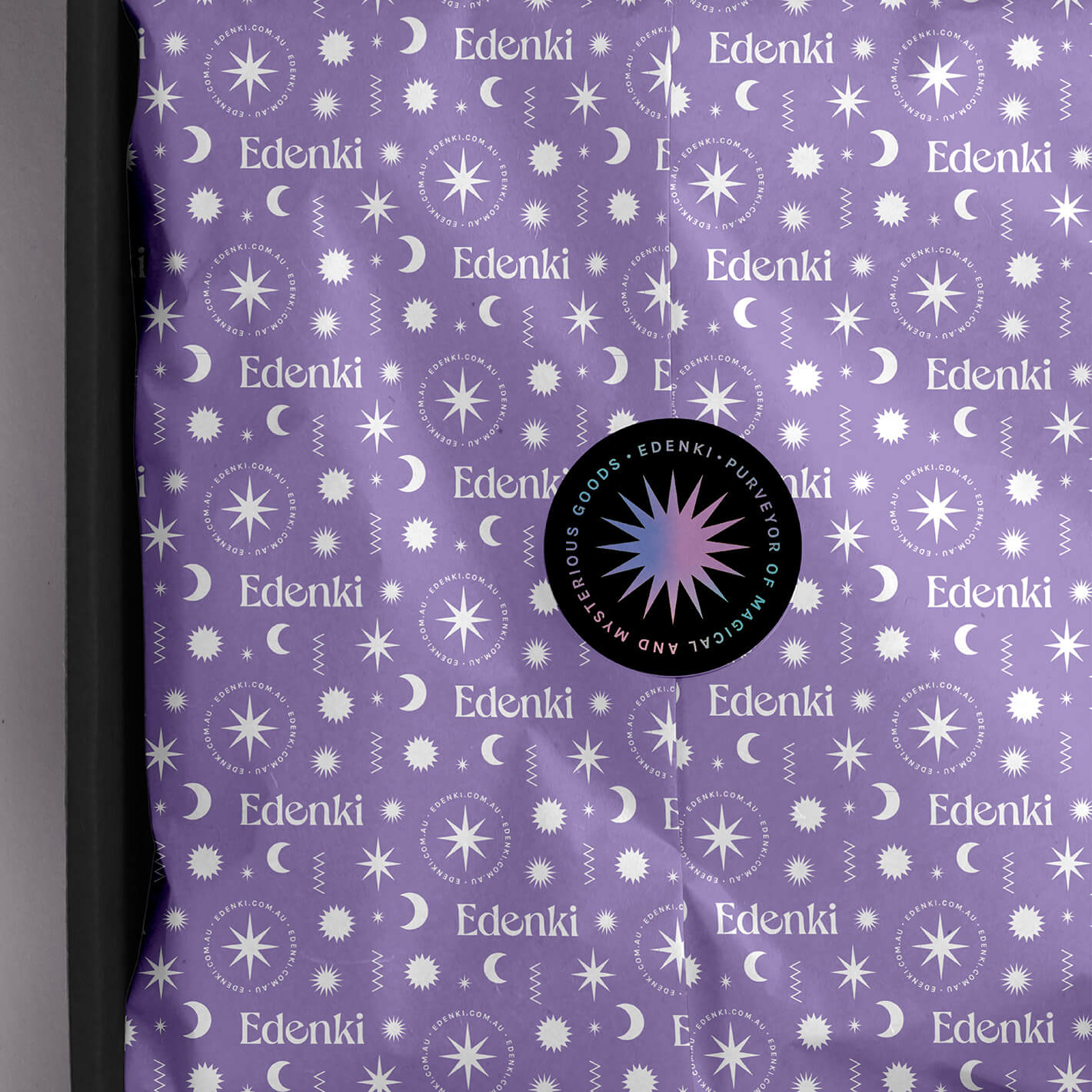 Brand identity case study image of the Edenki custom tissue paper in a box. The light purple design features the brand logo and supporting celestial icons in white with a black sticker with holographic foil sealing the package.