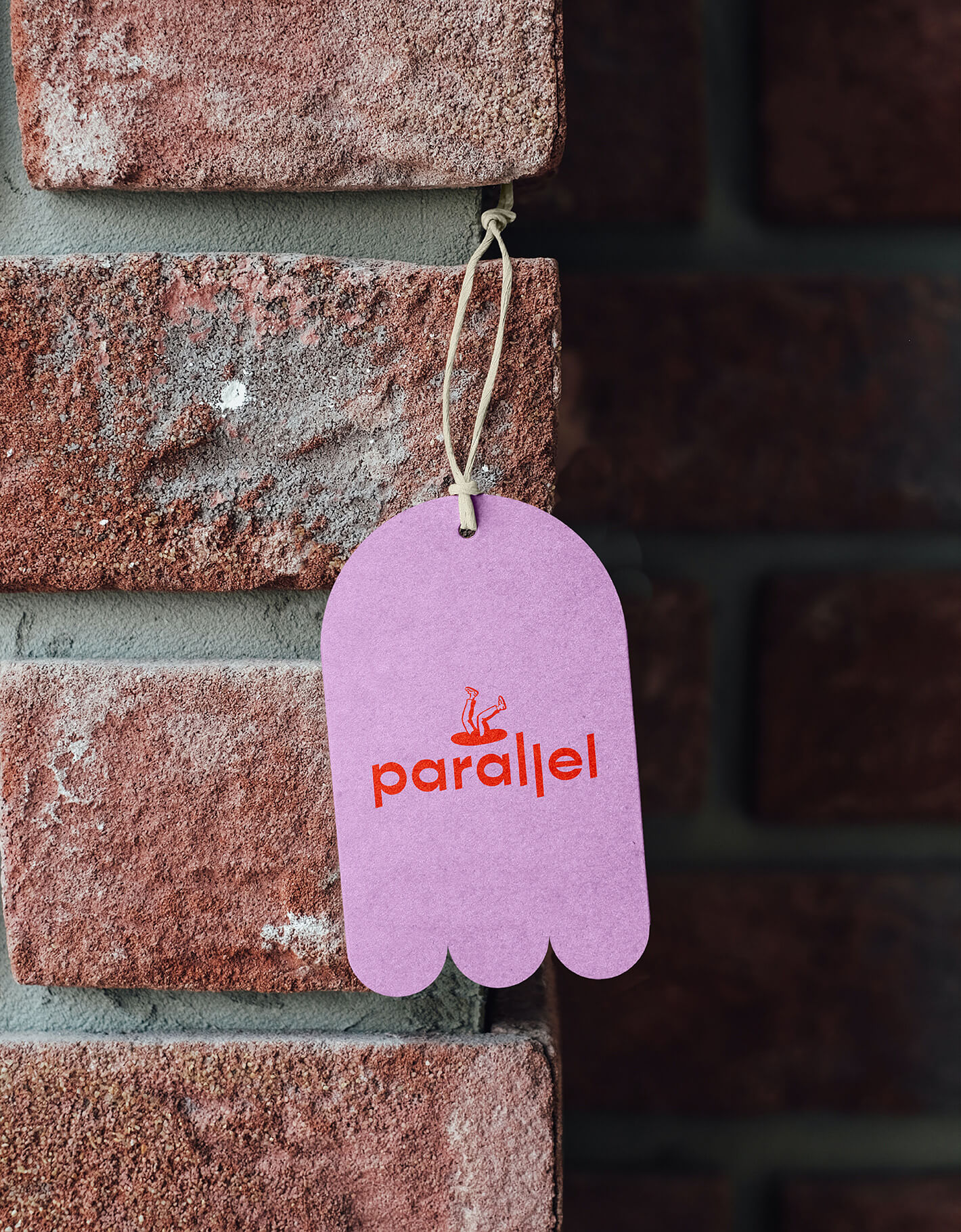 Rebranding case study image of Parallel swing tag on a brick wall. The tag is bright pink with a red logo as well as a custom-dieline in a blobby shape.
