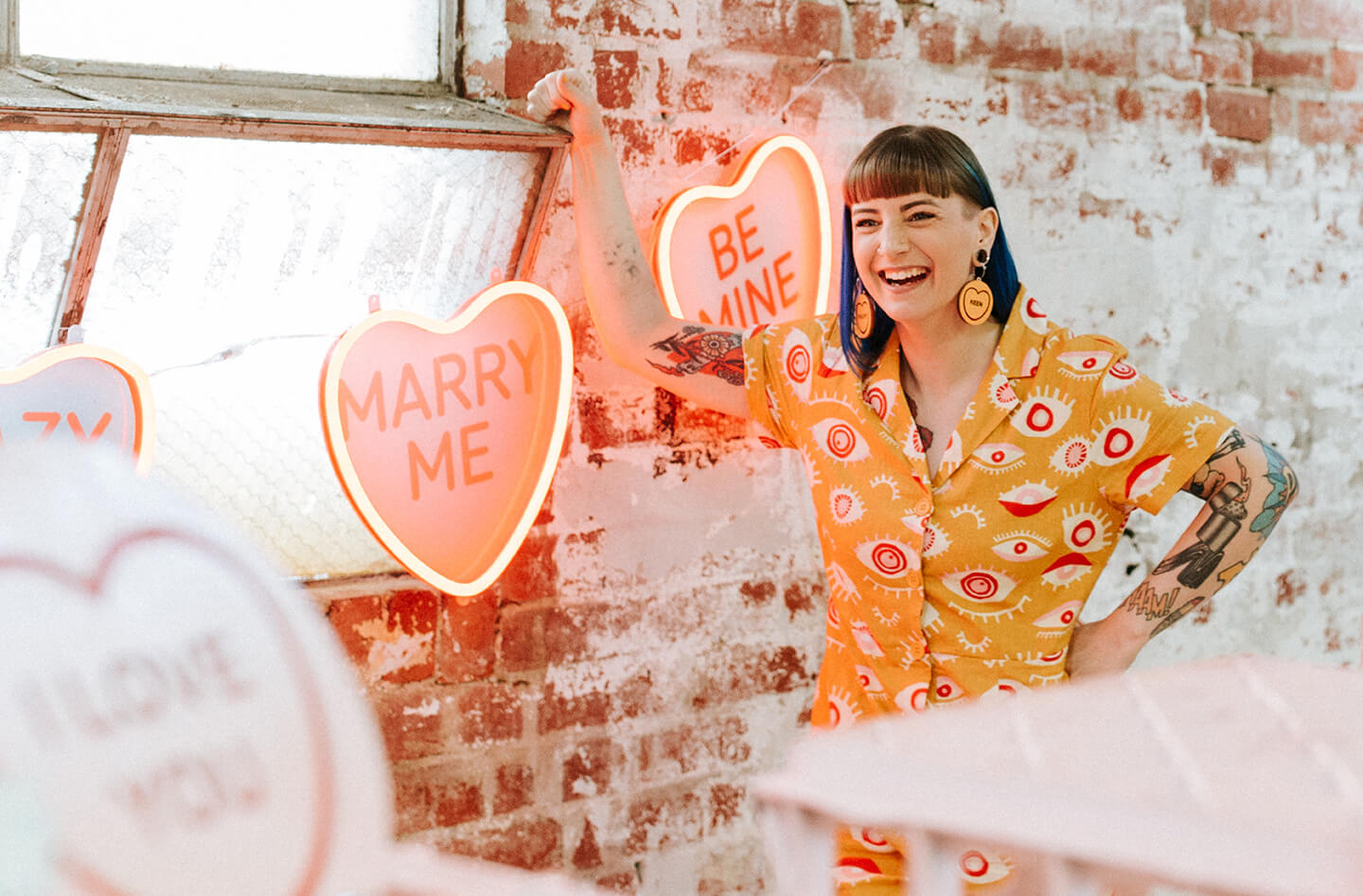 Brand identity case study image of founder Jess from Candy & Kitsch. She wears a colourful jumpsuit and stands in a sea of candy hearts and flowers.